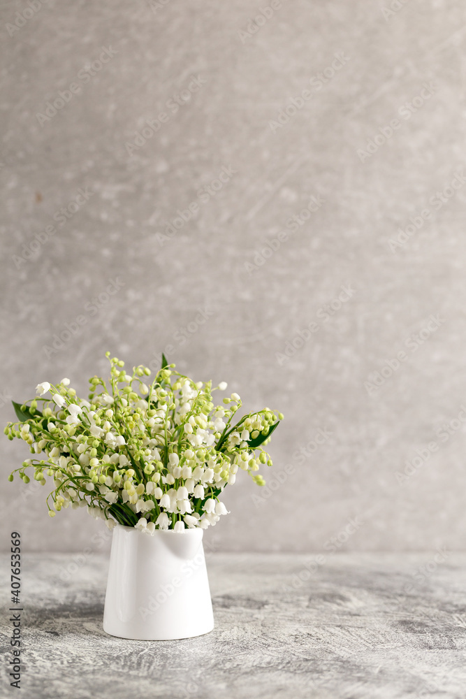 bouquet of lilies of the valley in a white glass on a gray concrete background