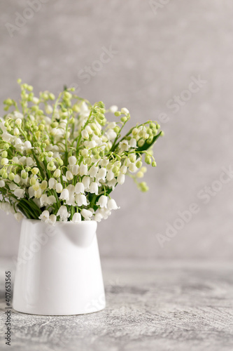 bouquet of lilies of the valley in a white glass on a gray concrete background