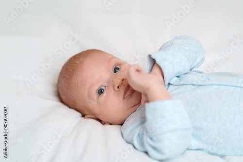 cute 2-month-old baby in blue bodysuit lies on bed and looks into frame