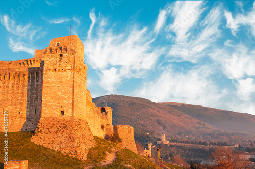 Close up view of medieval castle up the hill of Assisi, province in Umbria Italy. Stone bricks tower and walls at at sunset with clear clouds sky and tower in background