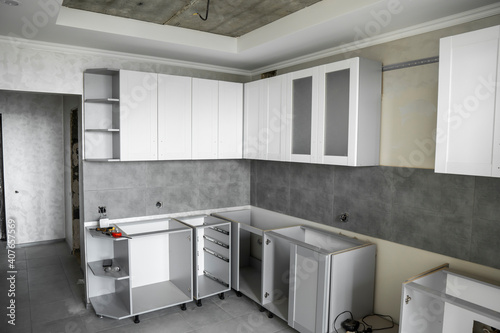 Custom kitchen cabinets installation with a white furniture facades mdf. Gray modular kitchen from chipboard material on a various stages of installation. A frame furniture fronts mdf profile.