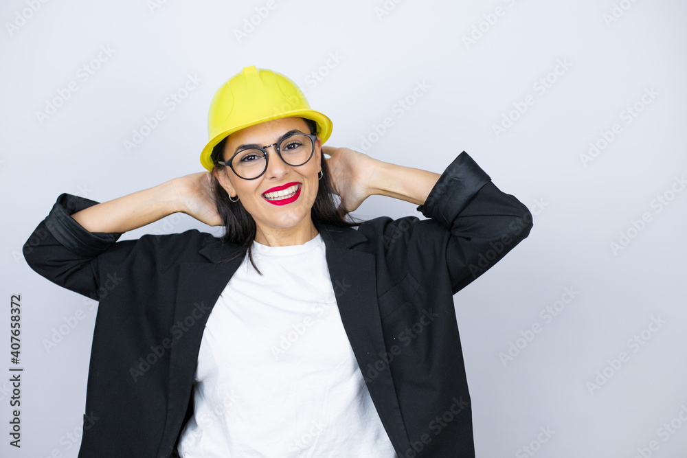 Young architect woman wearing hardhat relaxing and stretching, arms and hands behind head and neck smiling happy Young architect woman wearing hardhat relaxing and stretching, arms and hands behind head and neck smiling happy