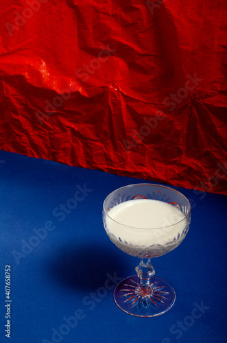 Old fashoned glass full of milk on the blue surface against red paper wall.Hard light and shadows photo