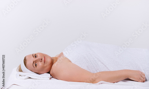 Caucasian senior woman in a white towel lies in the salon ready for spa treatments on a white background.