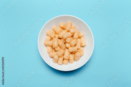 Top view of white bowl with corn puffs on blue background.