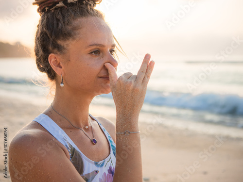 Woman's face close up. Yogi woman practicing Anuloma viloma Pranayama, Alternate Nostril Breathing. Breathing exercise. Self care concept. Sunset time. Yoga retreat. Thomas beach, Bali