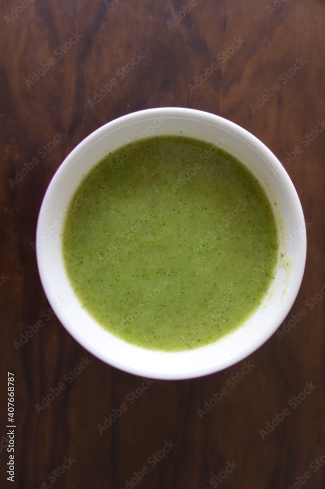spinach and zucchini cream into a white bowl on natural fiber background. Healthy food concept