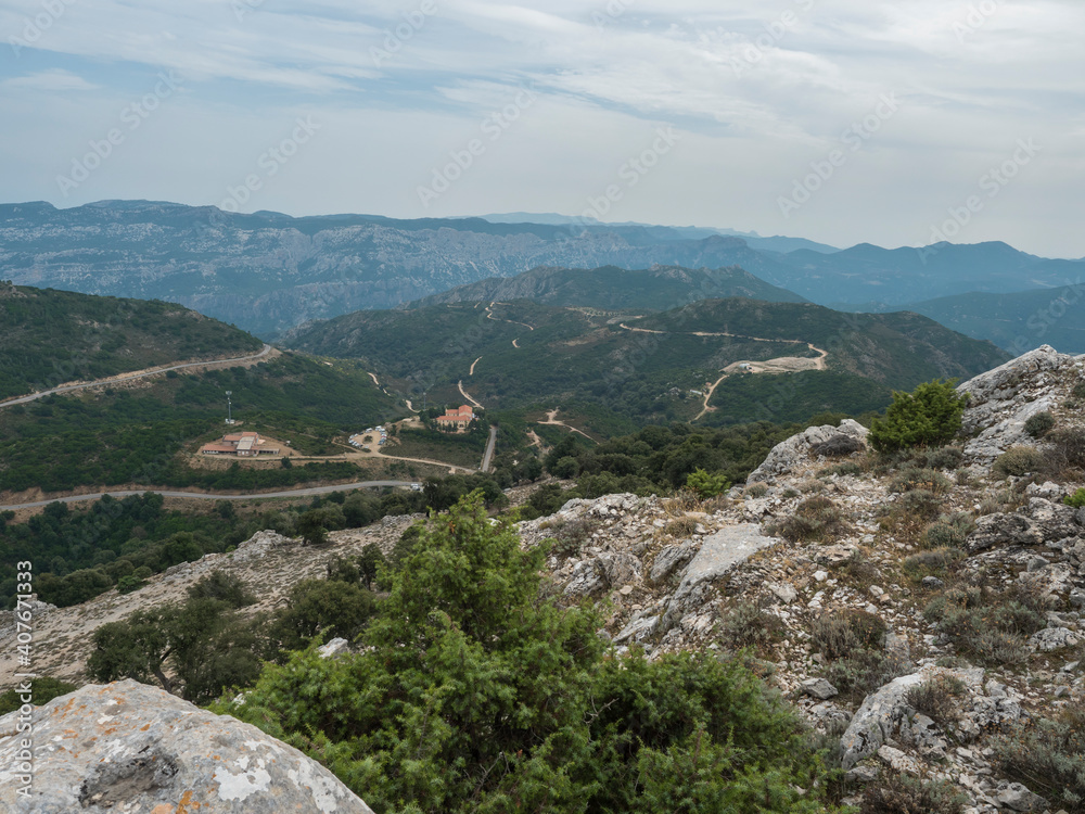 view of Supramonte Mountains with white limestone rock, green trees and Passo di Genna Silana in the valley. Sardinia, Italy. Summer cloudy day