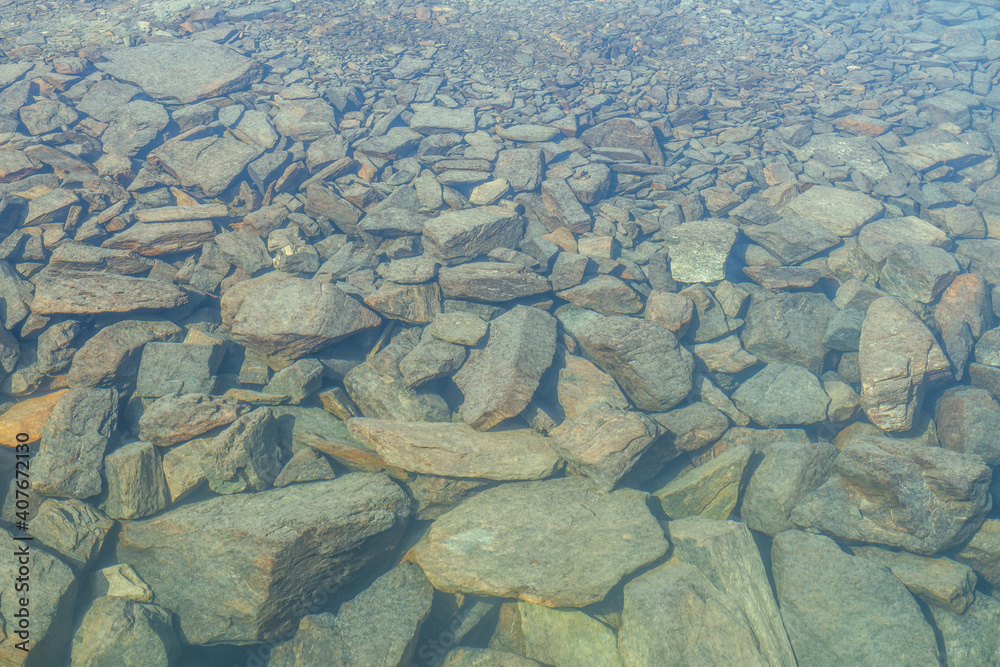 Beautiful nature background of stony bottom in transparent water of glacial lake in sunlight. Sunny nature backdrop with many stones in clear water of glacier lake. Invisible water of mountain lake. Beautiful nature background of stony bottom in transparent water of glacial lake in sunlight. Sunny nature backdrop with many stones in clear water of glacier lake. Invisible water of mountain lake.