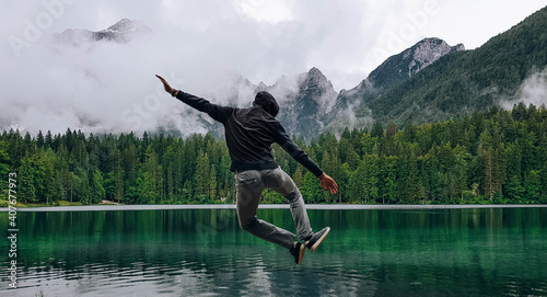 Canvas Print Shallow focus of a person jumping and heel kicking near a lake surrounded by roc