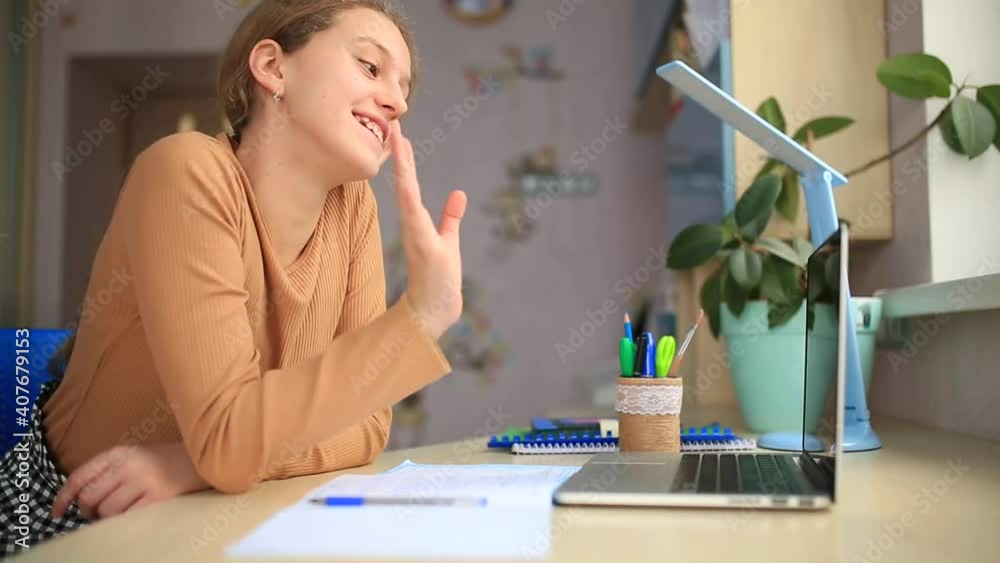 Beautiful schoolgirl waving to laptop screen having online class. Distance learning online education during coronavirus quarantine