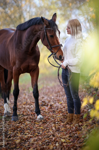 Young girl is standing with her horse on a forest path in autumn and the horse is sniffing at her sweater..