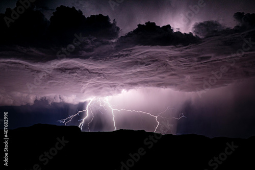 Powerful lightning storm in the American Southwest. One sees the silhouette of the hills on bottom, and moving up from there the lightning, cumulonimbus and the starry sky above. 