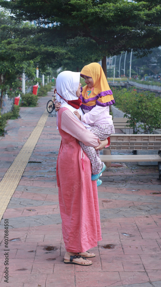 Portrait Asian muslim mother wearing hijab holding her child on the city park