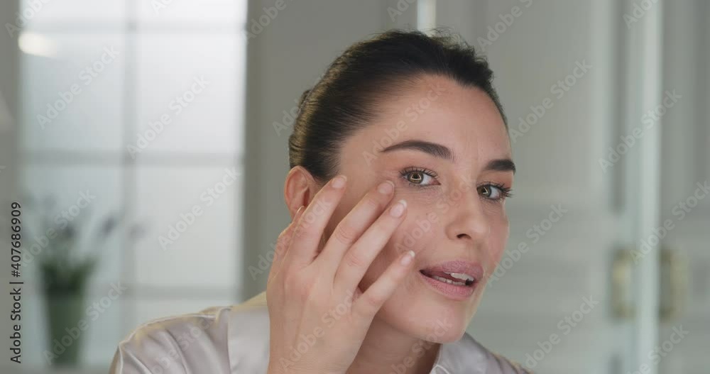 Beauty shot of mature woman applying foundation bb cream on previously applied moisturizing anti wrinkle face lotion and smiling in camera on golden background. Concept of skincare, cosmetics, make up Beauty shot of mature woman applying foundation bb cream on previously applied moisturizing anti wrinkle face lotion and smiling in camera on golden background. Concept of skincare, cosmetics, make up