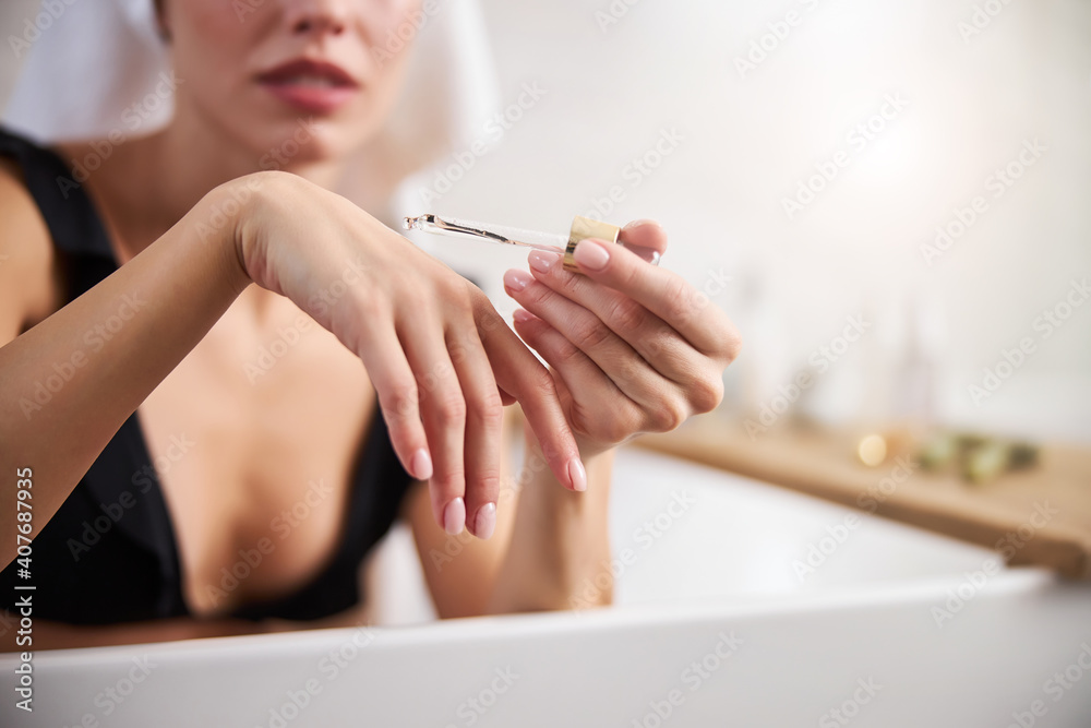 Fototapeta premium Calm young lady moisturizing her skin in the bathroom