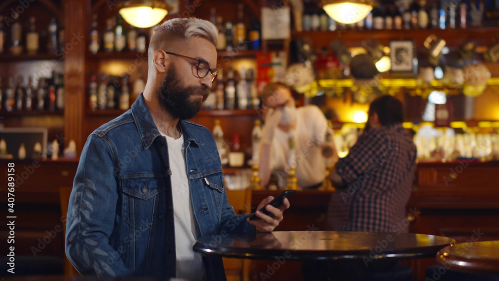 Bearded man texting on smartphone sitting at modern pub