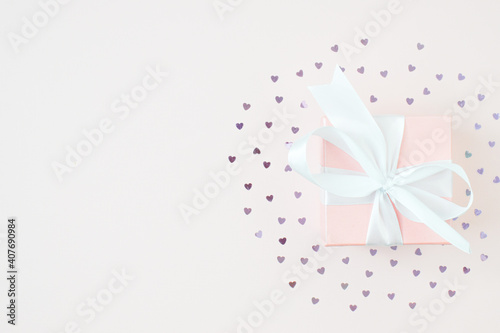 A gift box with a white bow on a pink background surrounded by hearts. © Irina Lesovaia