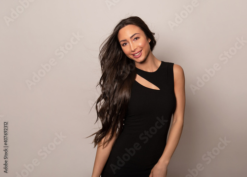 Beautiful young woman with long shiny black hair and natural make-up posing in dress on grey background 