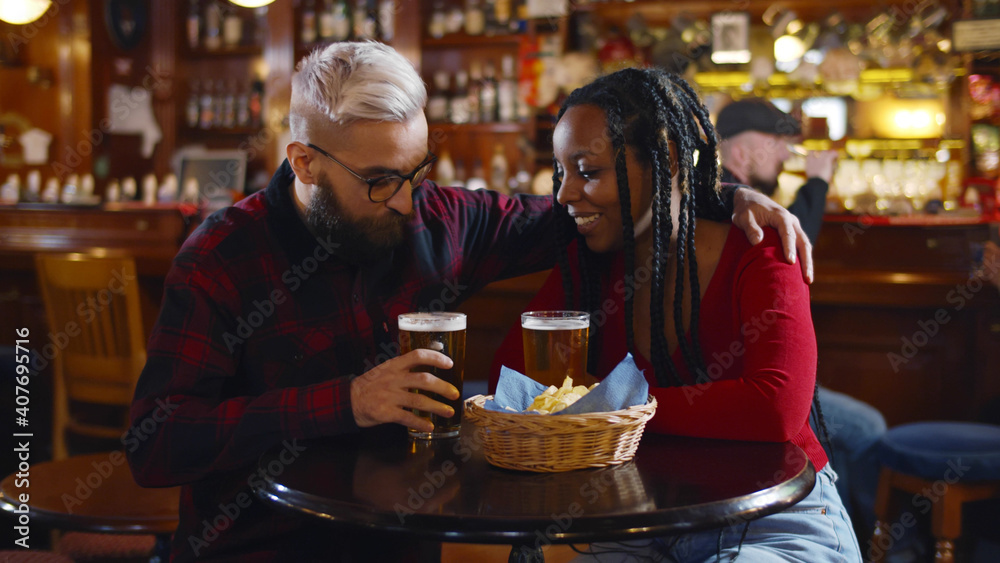 Diverse couple hugging having glass of beer in bar Diverse couple hugging having glass of beer in bar