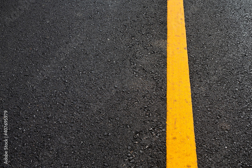 Close up black asphalt road surface texture with a yellow line. © Thawatchai