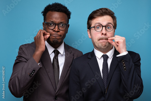 Canvas-taulu Two african and caucasian men shut mouth as zip with fingers