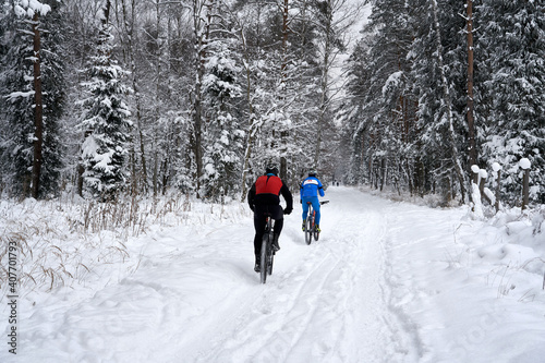 Two bicyclists riding their bikes in very cold winter day in Poland. Back view. Weekend in a snowy forest. 