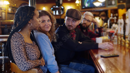 Cheerful diverse friends having fun and drinking draft beer at bar counter in pub.