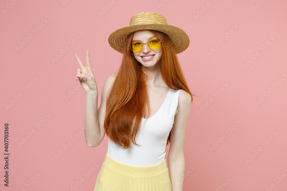 Young smiling lucky redhead cute gladden cheerful woman 20s ginger long hair wearing straw hat glasses summer clothes show victory v-sign gesture isolated on pastel pink background studio portrait.