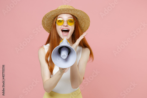 Young redhead ginger surprised caucasian woman 20s wearing straw hat glasses summer clothes sreaming loudly shouting in megaphone spread hand isolated on pastel pink color background studio portrait photo