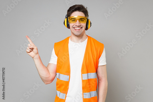 Φωτογραφία Young employee happy handyman man in orange vest protective ear muffs point index finger aside on copy space isolated on grey background studio