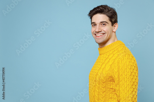 Side profile view of young caucasian attractive smiling unshaved student man 20s wearing casual knitted cozy yellow fashionable sweater look camera isolated on blue color background studio portrait. photo