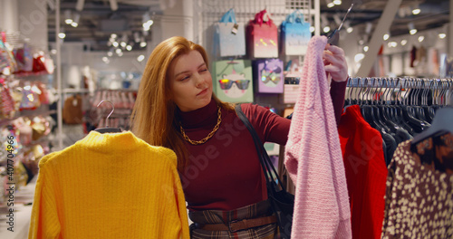 Young lady standing in clothes shop indoors choosing sweater