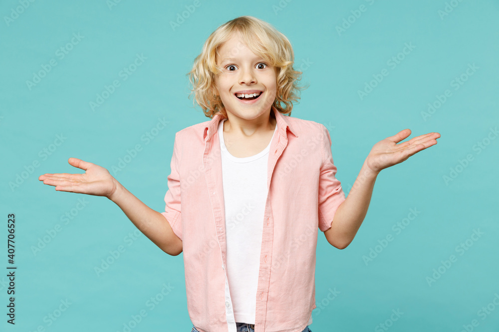Surprised little curly kid boy 10s years old wearing pastel pink shirt spreading hands looking camera isolated on blue turquoise color background children studio portrait. Childhood lifestyle concept. Surprised little curly kid boy 10s years old wearing pastel pink shirt spreading hands looking camera isolated on blue turquoise color background children studio portrait. Childhood lifestyle concept.