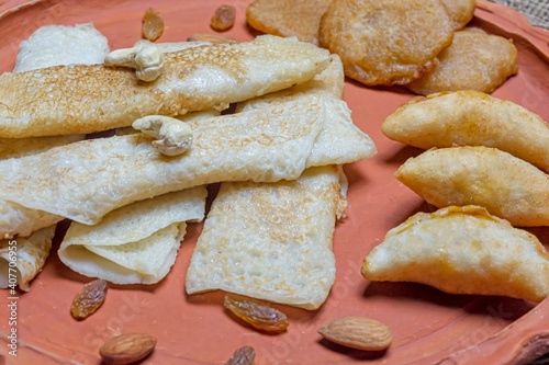 Bengali sweet - Patishapta Pitha, Malpua and Puli Pitha in a earthenware plate on wooden background with cashew nut, almonds and raisins. photo