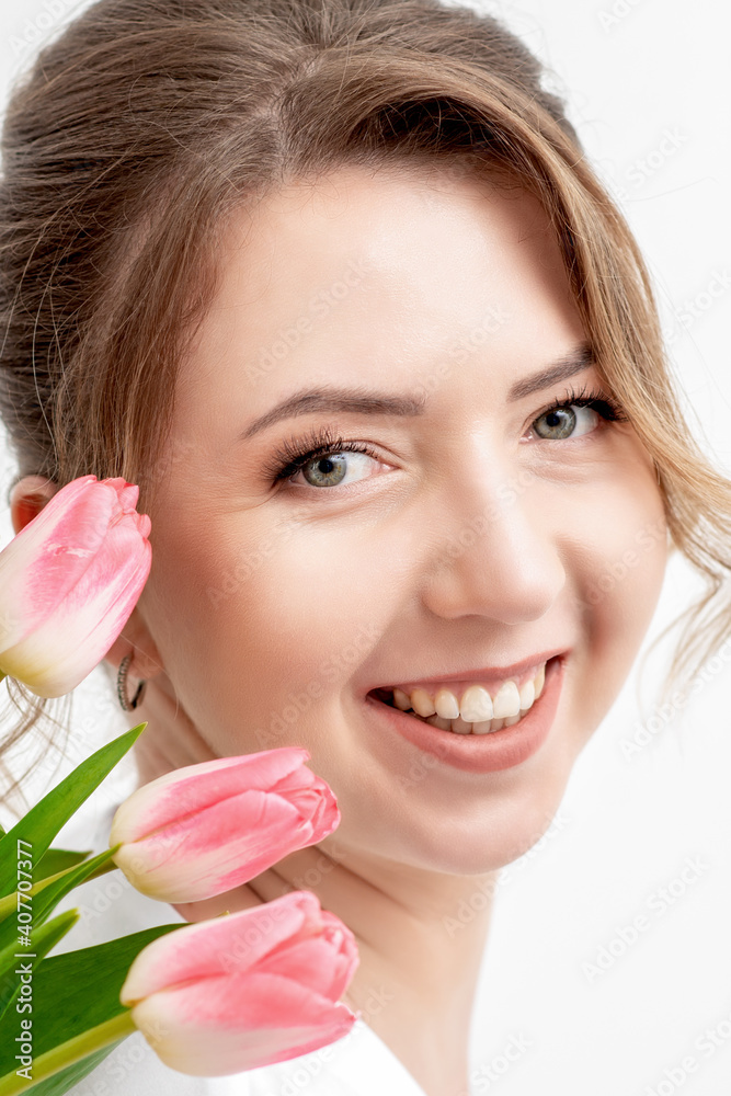 Portrait of a happy young caucasian woman with pink tulips against a white background