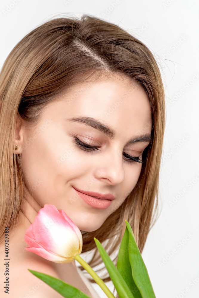 A portrait of a happy young caucasian woman with closed eyes and one pink tulip against a white background with copy space