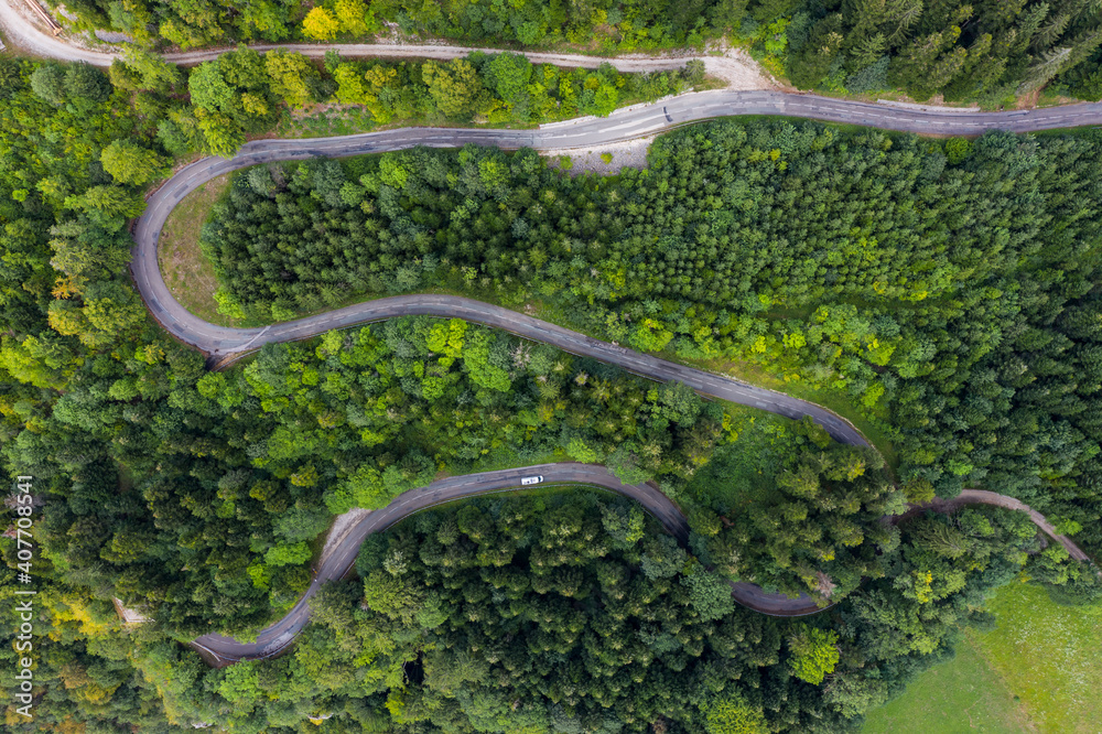 Aerial view of a winding countryside road passing through the green forest and mountain. White camping cars are passing through. Aerial view of a winding countryside road passing through the green forest and mountain. White camping cars are passing through.