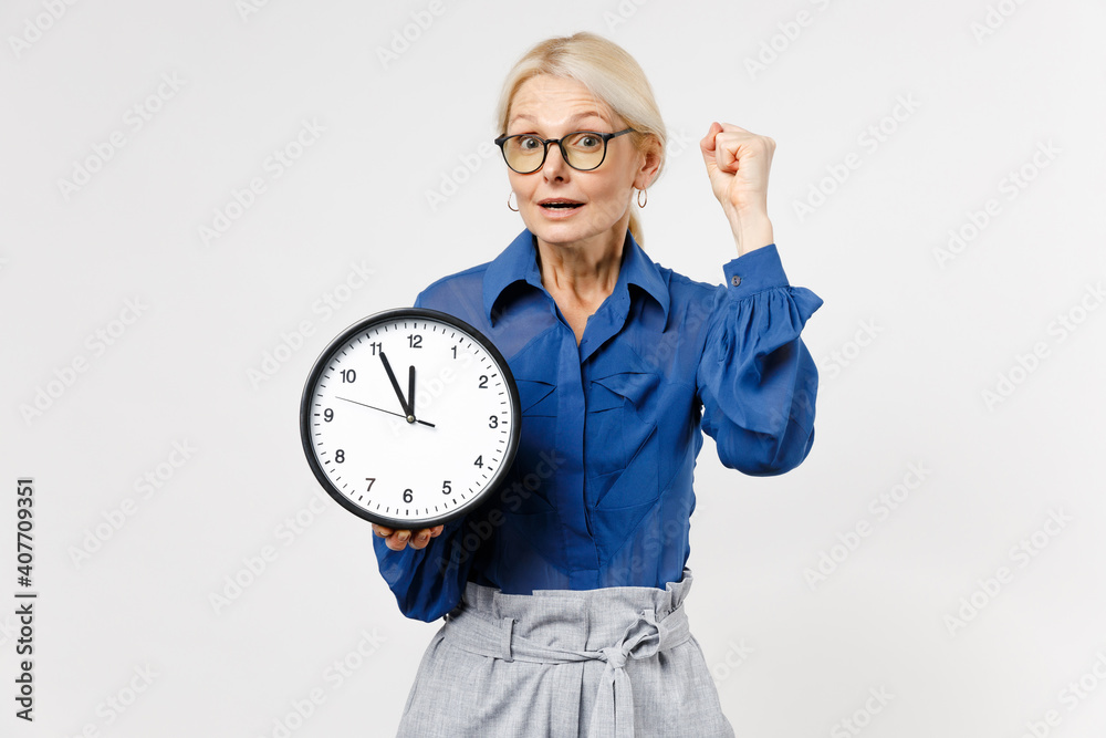 Blonde confident business woman 40s in blue shirt glasses formal clothes holding in hands clock do winner gesture clenching fist clisolated on white background studio portrait Time management concept Blonde confident business woman 40s in blue shirt glasses formal clothes holding in hands clock do winner gesture clenching fist clisolated on white background studio portrait Time management concept