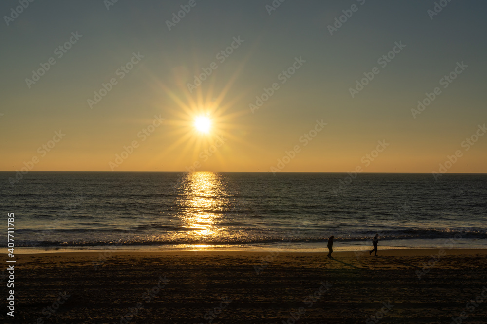 people enjoy an evening walk on an empty golden sand beach at sunset