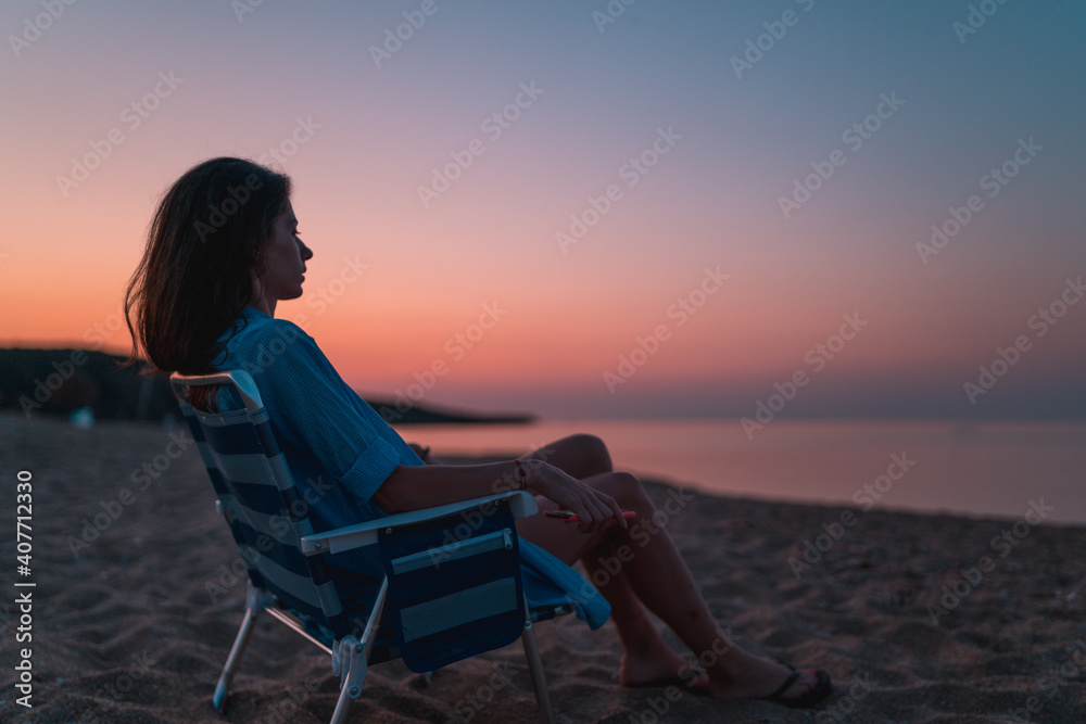 Relaxed Beautiful young woman sitting on chair on beach and watching sunset