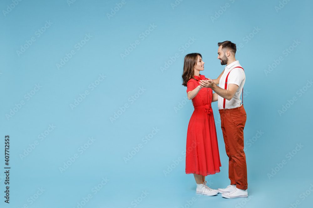 Full length smiling young couple two friends man woman in white red clothes dancing looking at each other isolated on pastel blue color background studio portrait. St. Valentine's Day holiday concept. Full length smiling young couple two friends man woman in white red clothes dancing looking at each other isolated on pastel blue color background studio portrait. St. Valentine's Day holiday concept.