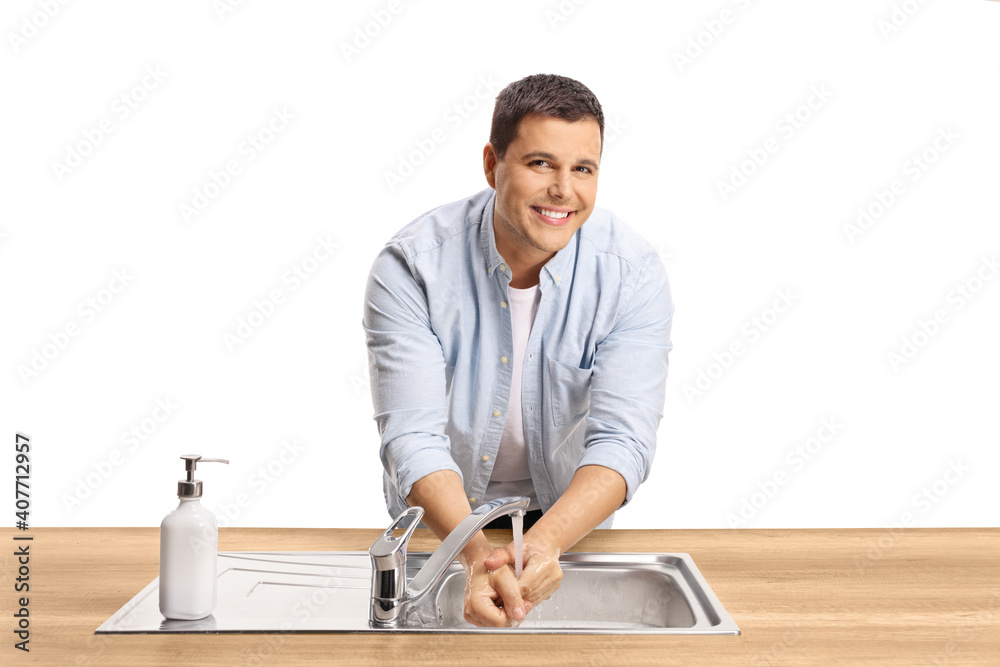 Young casual man washing hands in a sink on a wooden counter and looking at camera Young casual man washing hands in a sink on a wooden counter and looking at camera