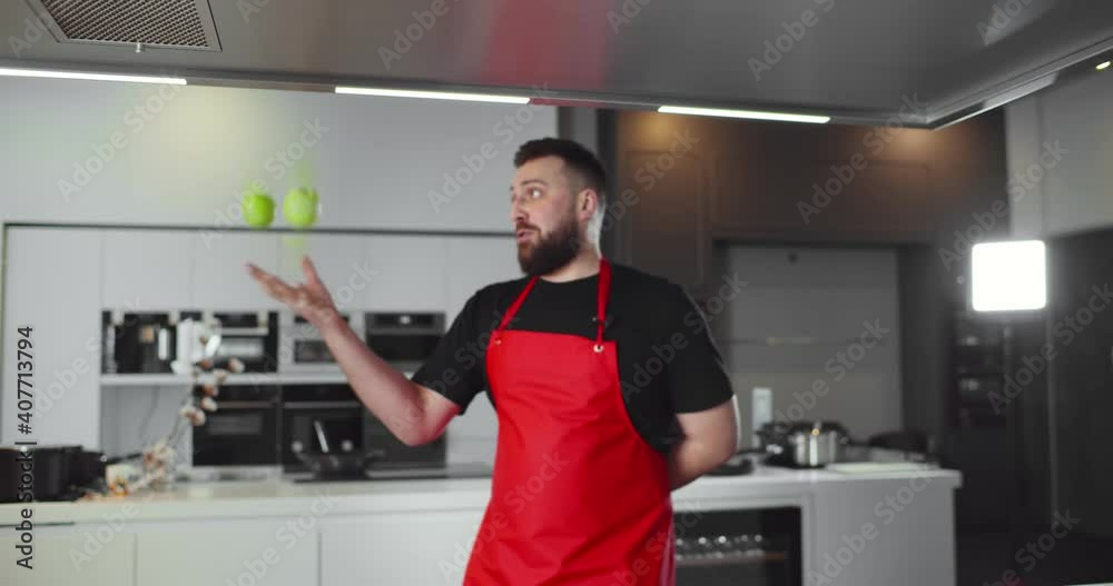 Man chef juggling apples with one hand and dropping them cooking in modern kitchen Man chef juggling apples with one hand and dropping them cooking in modern kitchen