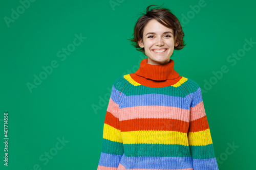 Smiling cheerful beautiful attractive young brunette woman 20s years old wearing basic casual colorful sweater standing and looking camera isolated on bright green color background studio portrait.