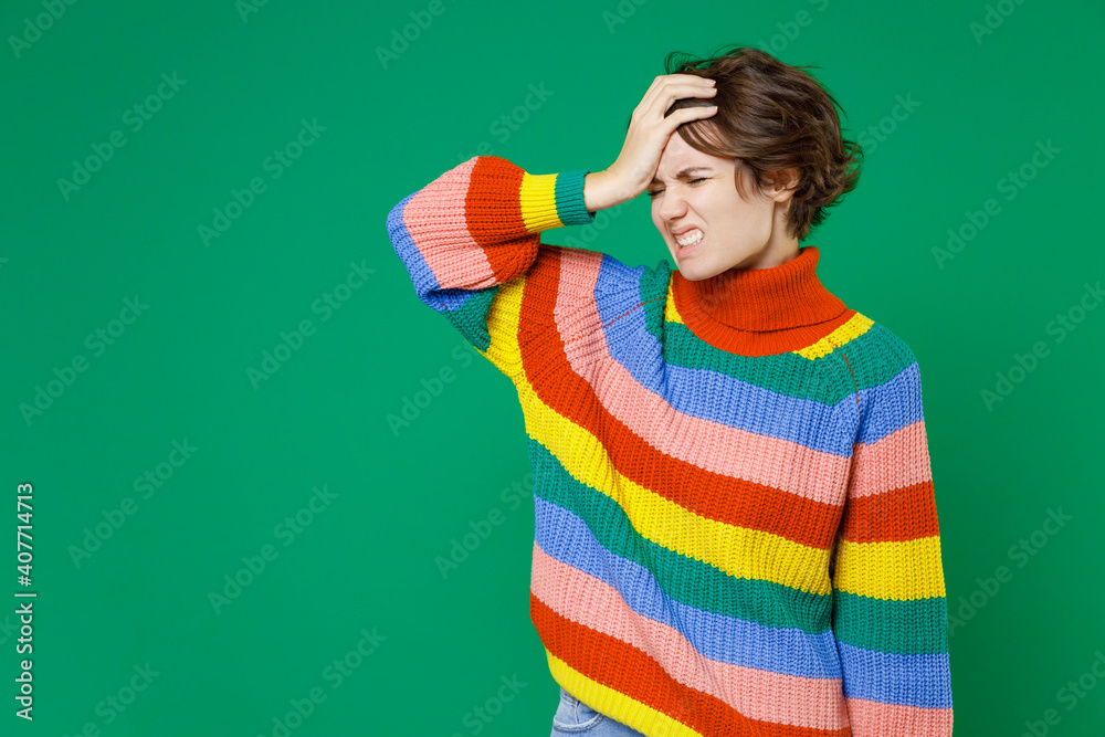 Sick exhausted tired young brunette woman 20s years old in colorful sweater standing put hand on head keeping eyes closed having headache isolated on bright green color background studio portrait. Sick exhausted tired young brunette woman 20s years old in colorful sweater standing put hand on head keeping eyes closed having headache isolated on bright green color background studio portrait.