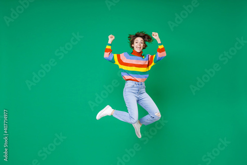 Full length of happy joyful young brunette woman 20s years old wearing basic casual colorful sweater jumping doing winner gesture celebrating isolated on bright green color background studio portrait.