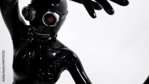 Close-up of a woman dressed in a tight black latex suit for a BDSM role-playing game, she is on a white background in the studio.