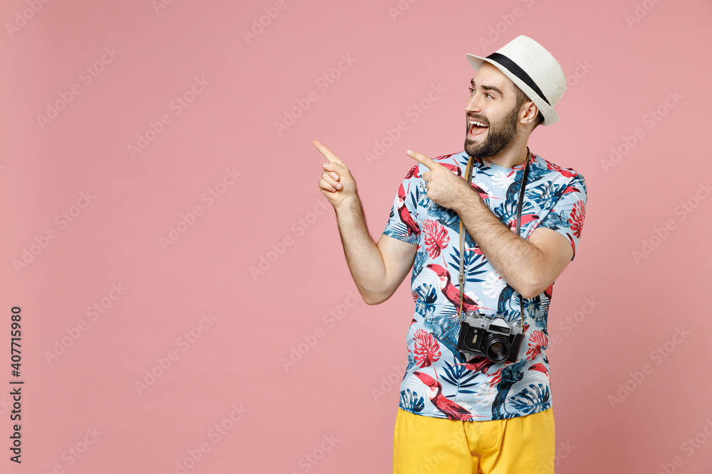 Excited young traveler tourist man in summer clothes hat with photo camera point index fingers aside up isolated on pink background. Passenger traveling abroad on weekends. Air flight journey concept. Excited young traveler tourist man in summer clothes hat with photo camera point index fingers aside up isolated on pink background. Passenger traveling abroad on weekends. Air flight journey concept.