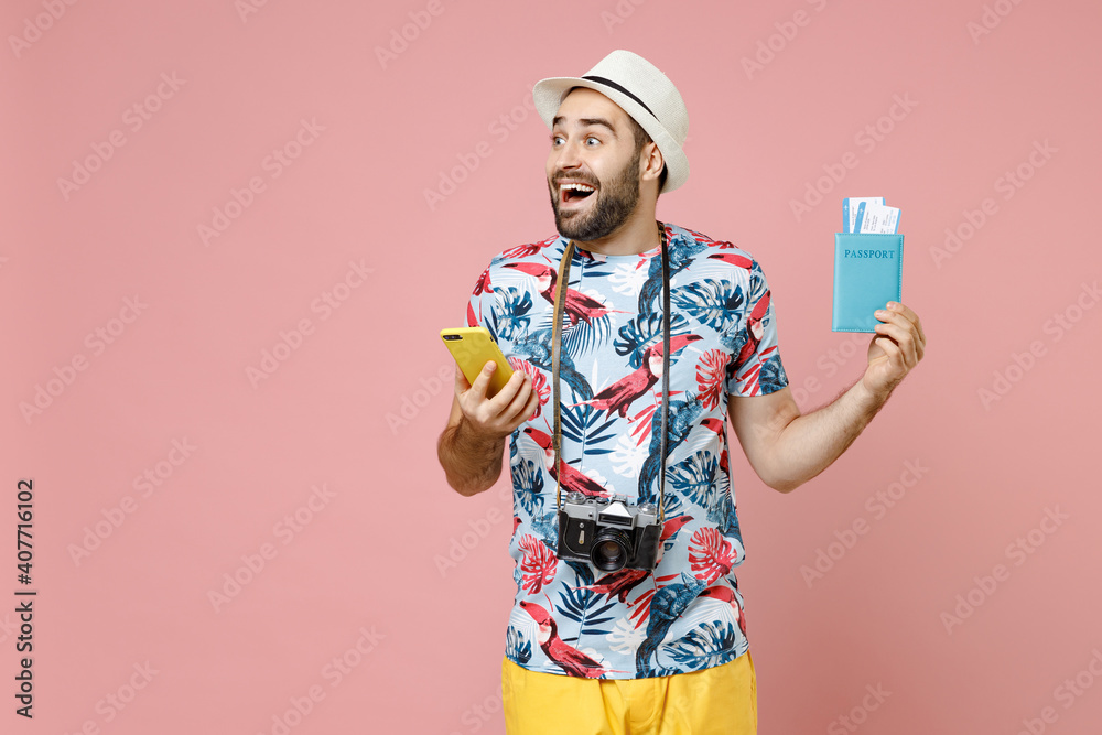 Excited young traveler tourist man in summer clothes hat using mobile cell phone hold passport tickets isolated on pink background. Passenger traveling abroad on weekends. Air flight journey concept. Excited young traveler tourist man in summer clothes hat using mobile cell phone hold passport tickets isolated on pink background. Passenger traveling abroad on weekends. Air flight journey concept.